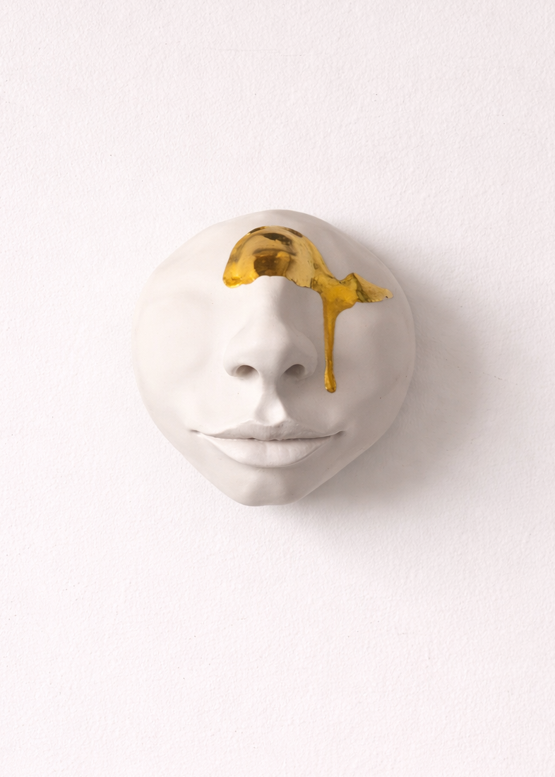 Porcelain wall art of a face with gold accents on a white background